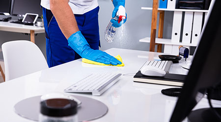 Professional cleaner disinfecting office desk surface in North York